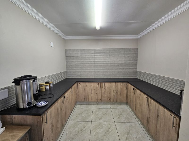 A clean and functional kitchenette area featuring modern wood-look cabinetry, dark countertops, and neutral tiled flooring, suitable for office staff use.