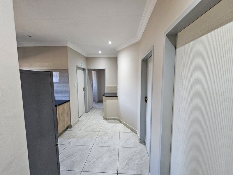 A clean, well-maintained hallway featuring neutral tiled flooring, recessed lighting, and access to multiple office rooms with built-in cabinetry.