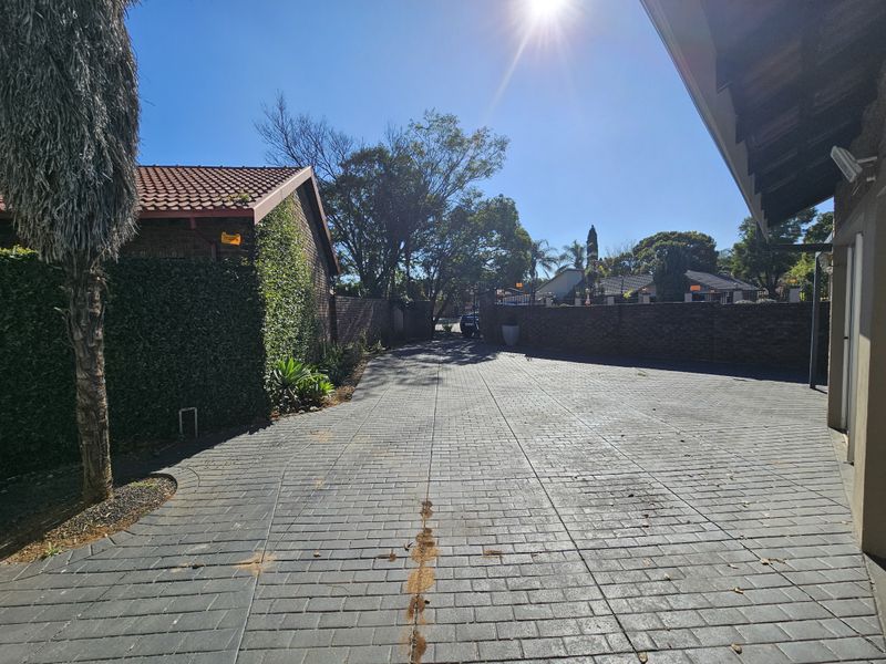 A paved driveway leading to the property entrance, featuring brick boundary walls and mature landscaping under a clear sky.
