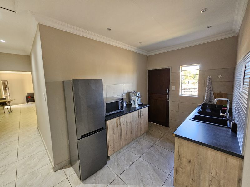 A functional office kitchen featuring modern wood-look cabinetry, dark laminate countertops, a double basin sink, and tiled flooring with recessed lighting.