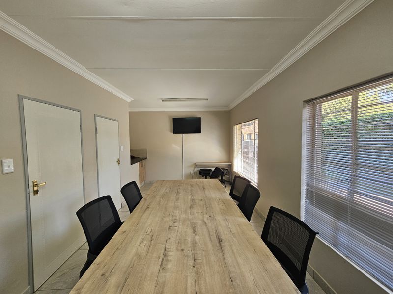 A functional office space featuring tiled flooring, coving, and large windows with venetian blinds, suitable for a professional meeting or workspace environment.
