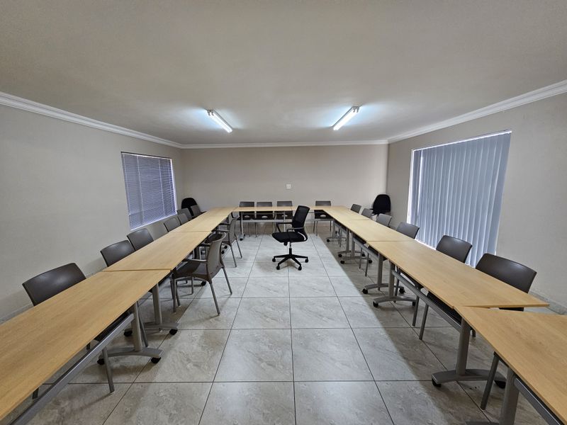 A functional office meeting room featuring tiled flooring, neutral walls, and dual window treatments including vertical and venetian blinds.