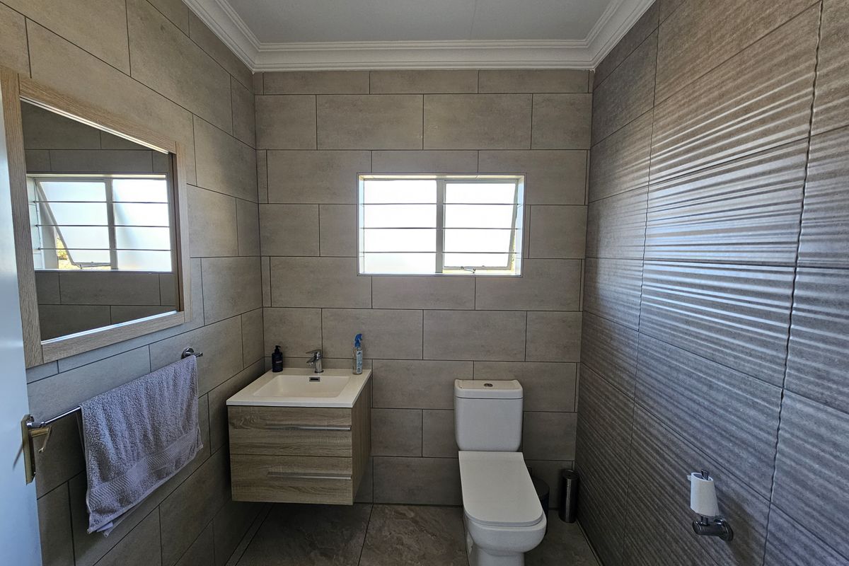 A modern, well-maintained bathroom featuring neutral-toned wall and floor tiles, a wall-mounted vanity with a basin, and a contemporary toilet.