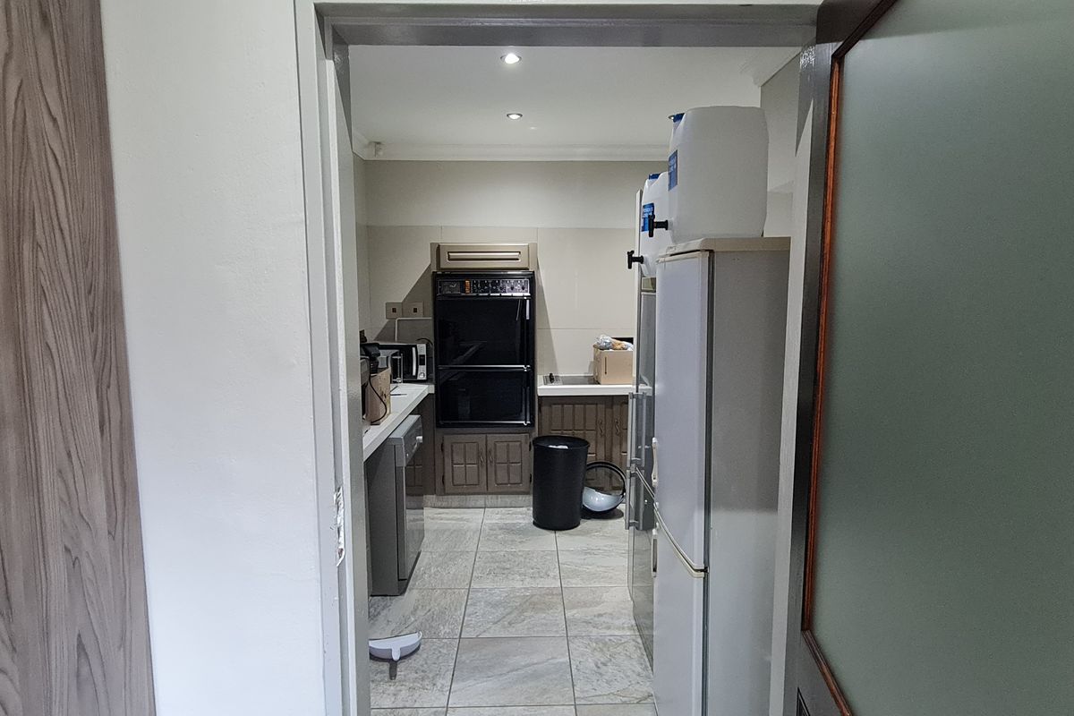 A functional office kitchen area featuring built-in cabinetry, a double oven, and tiled flooring, viewed from the adjacent hallway.