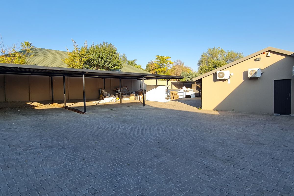 Spacious paved exterior area featuring a large covered carport structure and multiple wall-mounted air conditioning units on the office building facade.