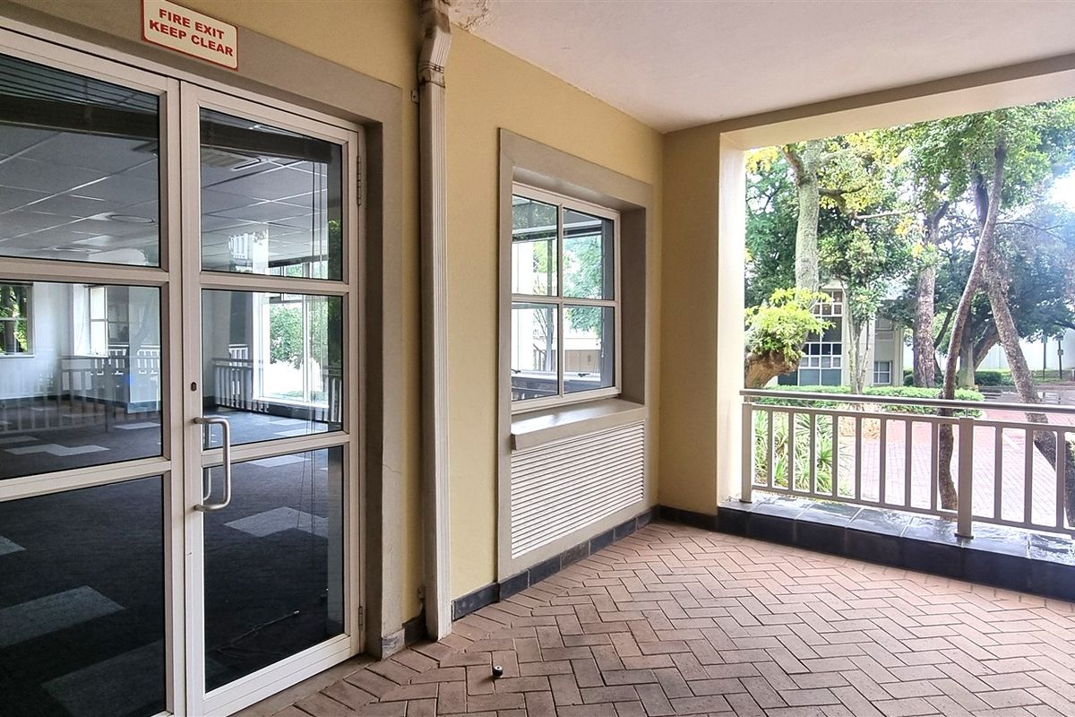 A covered outdoor patio area featuring brick paving, metal railings, and direct access to the office interior through a glass double door.