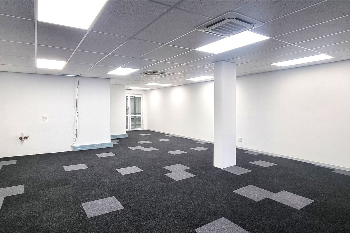 A spacious, open-plan office area featuring a suspended ceiling with recessed lighting, central air conditioning, and modern carpet tiles.