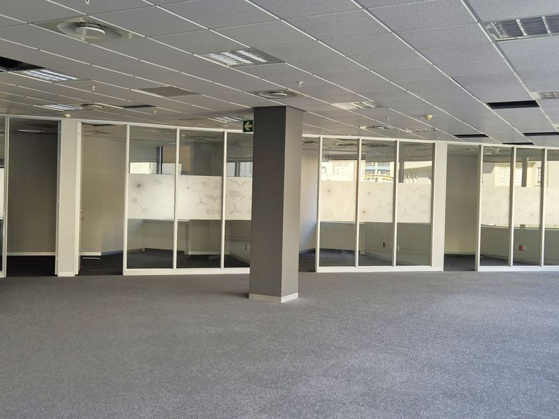 Open plan office space featuring glass partitioned rooms, suspended ceilings, and carpeted flooring, offering a flexible layout for professional use.