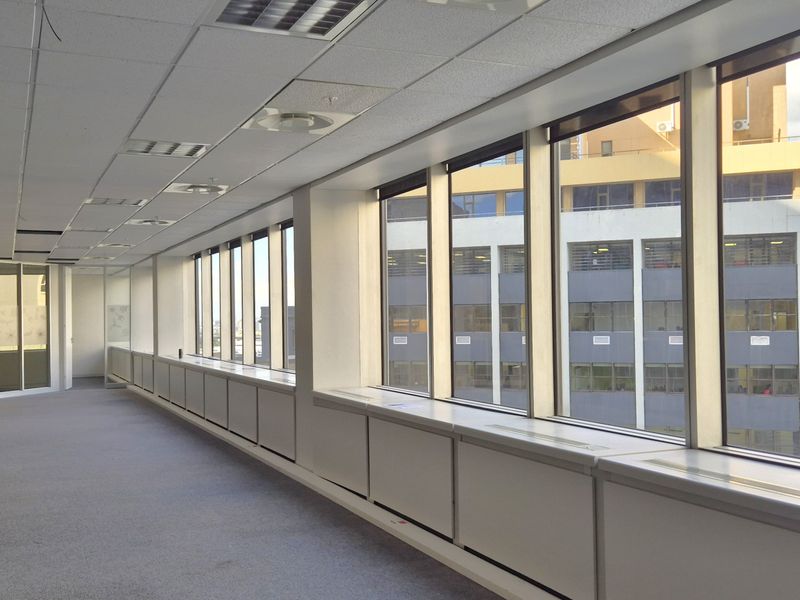 Spacious, empty open-plan office area featuring large windows with city views, suspended ceilings, and glass partitions, offering a bright and professional workspace.