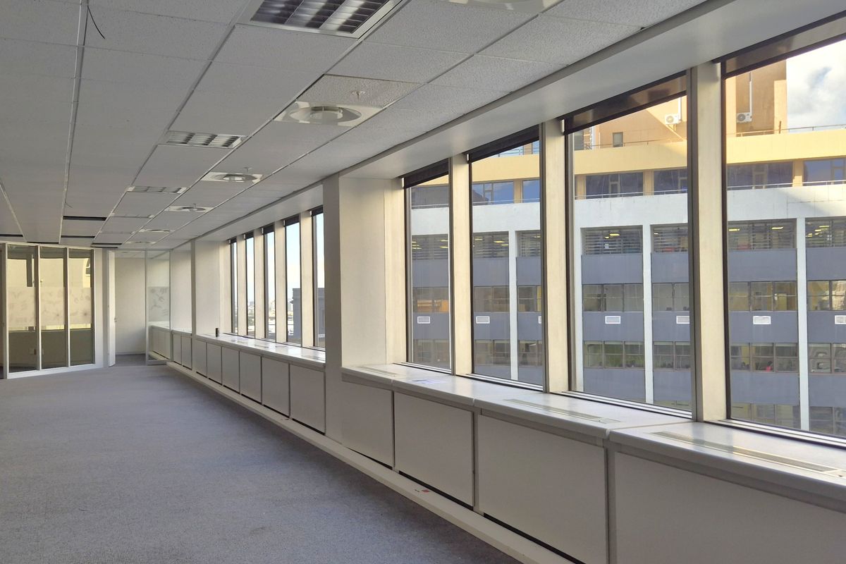 Spacious, empty open-plan office area featuring large windows with city views, suspended ceilings, and glass partitions, offering a bright and professional workspace.