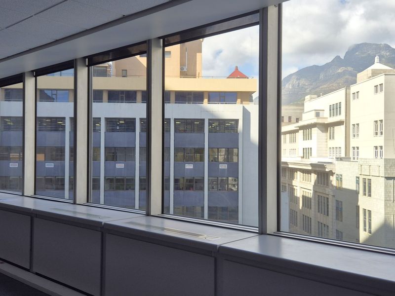 A bright, empty office space featuring expansive floor-to-ceiling windows with city and mountain views, suspended ceilings, and integrated perimeter climate control units.