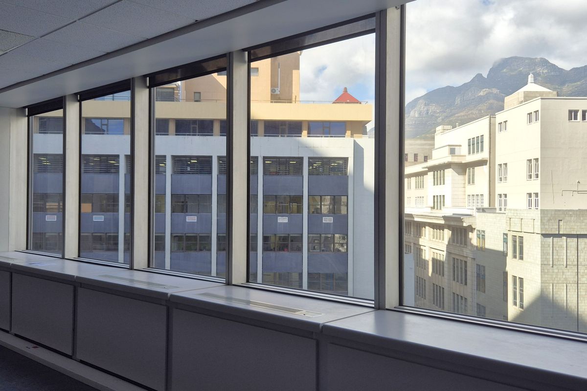 A bright, empty office space featuring expansive floor-to-ceiling windows with city and mountain views, suspended ceilings, and integrated perimeter climate control units.