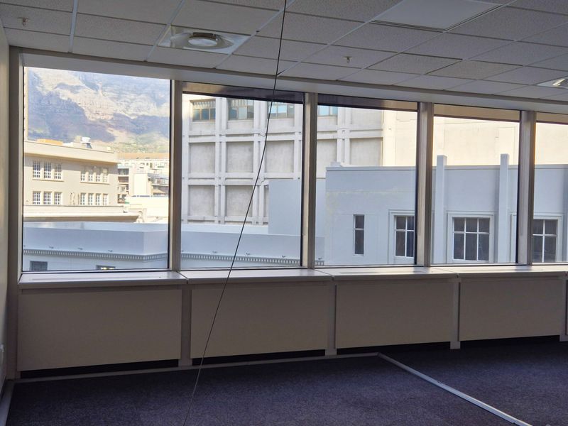 An empty, carpeted office space featuring large windows with city and mountain views, suspended ceilings, and integrated HVAC systems.