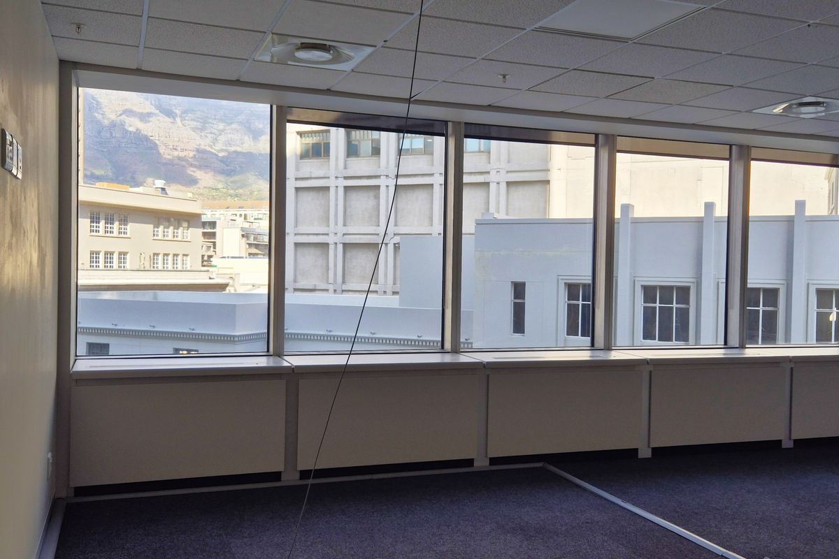 An empty, carpeted office space featuring large windows with city and mountain views, suspended ceilings, and integrated HVAC systems.
