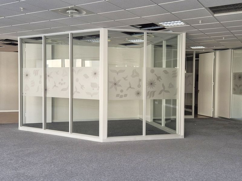 Open plan office space featuring glass partitioned meeting rooms, carpeted flooring, and a suspended ceiling with integrated lighting and air conditioning.