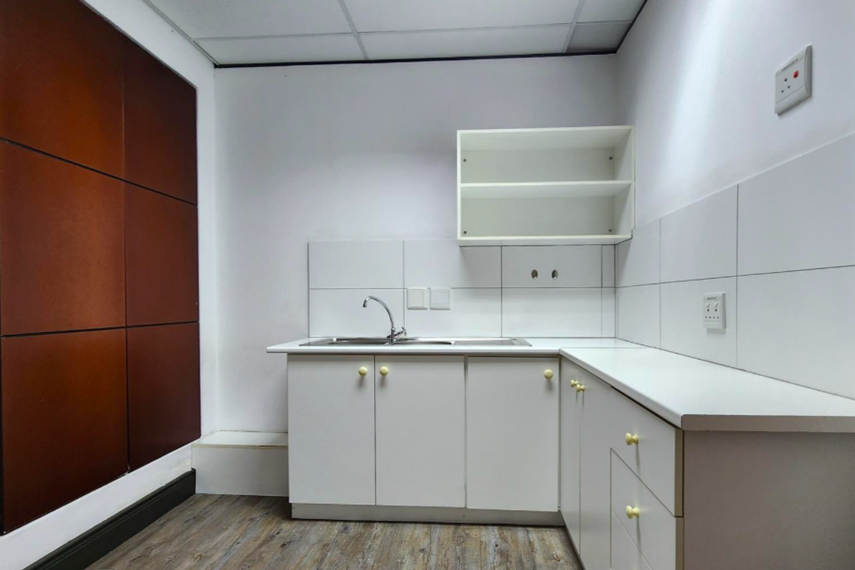 A compact office kitchenette featuring white cabinetry, a stainless steel sink, tiled backsplash, and wood-look flooring.