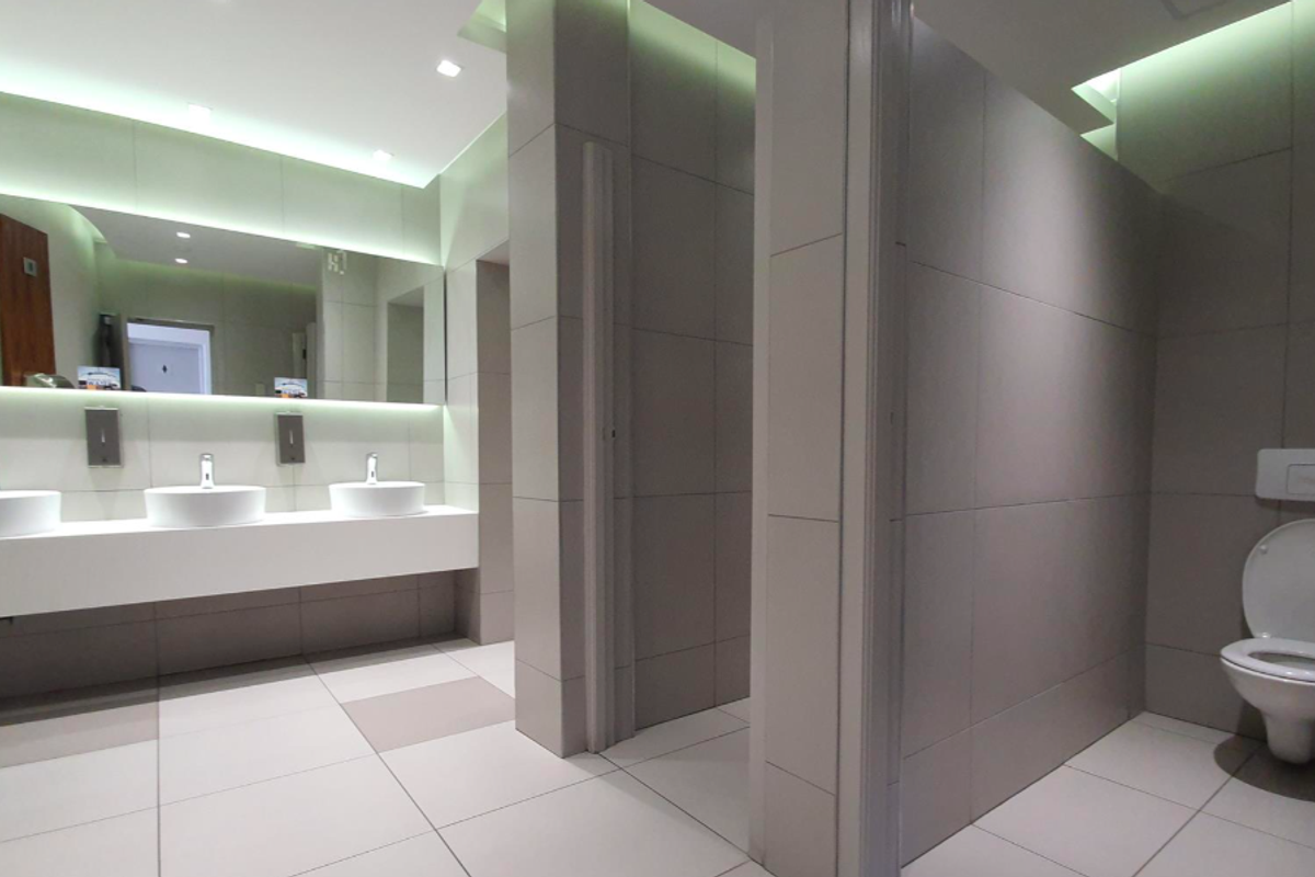 Modern office restroom featuring three vessel sinks on a floating vanity, recessed lighting, and private toilet cubicles with wall-mounted toilets.