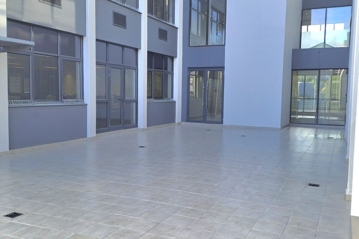 A spacious, paved outdoor courtyard area situated between modern office building wings, featuring large glass windows and secure access points.