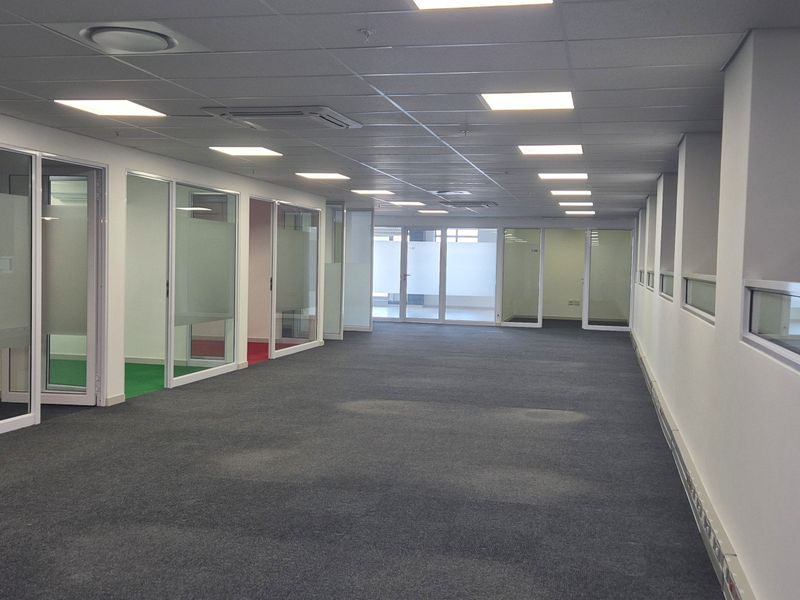 Spacious open-plan office area featuring glass-partitioned private offices, recessed ceiling lighting, and integrated air conditioning units.