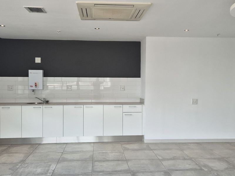 A clean, modern office kitchenette featuring white cabinetry, subway tile backsplash, stainless steel sink, and integrated ceiling air conditioning unit.