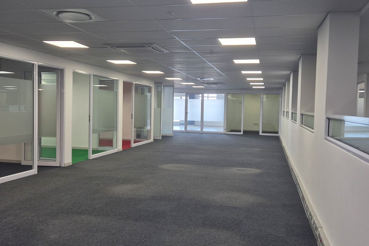 Spacious open-plan office area featuring glass-partitioned private offices, recessed ceiling lighting, and integrated air conditioning units.