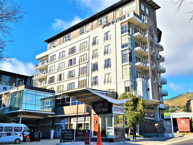A modern multi-story office and hotel building featuring a glass facade, private balconies, and a dedicated porte cochere entrance with security.