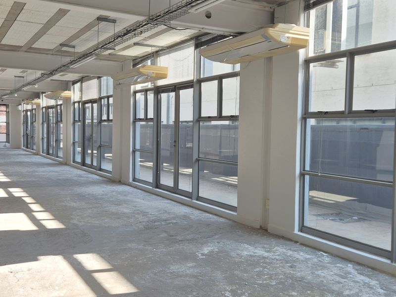 Spacious open-plan office area featuring large windows, exposed industrial-style ceilings, and wall-mounted air conditioning units, providing a blank canvas for custom fit-outs.
