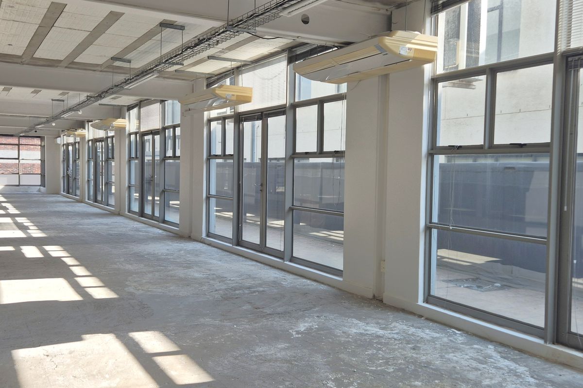 Spacious open-plan office area featuring large windows, exposed industrial-style ceilings, and wall-mounted air conditioning units, providing a blank canvas for custom fit-outs.