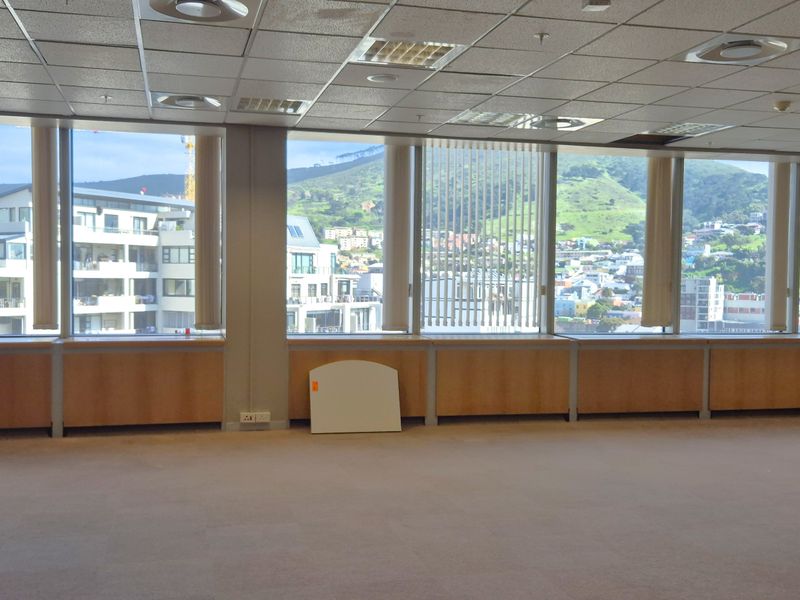 Spacious, empty office area featuring a suspended ceiling, carpeted floors, and expansive windows offering panoramic city and mountain views.
