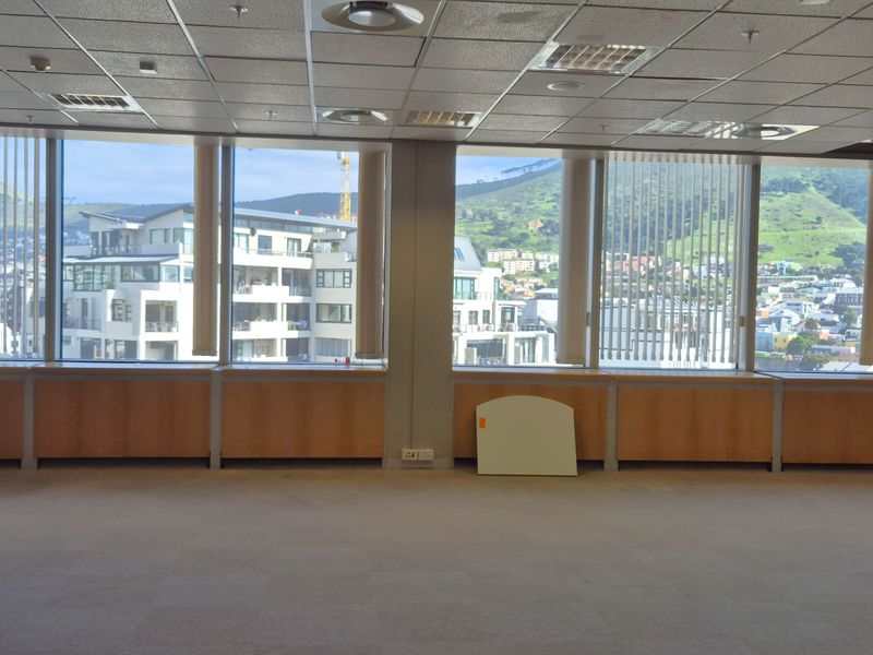 Spacious empty office area featuring large floor-to-ceiling windows with city views, suspended ceiling, and built-in wooden cabinetry along the perimeter.