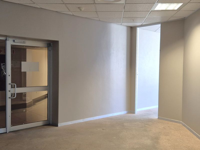 A vacant office space featuring neutral walls, a suspended ceiling with recessed lighting, and an aluminium-framed glass entrance door.