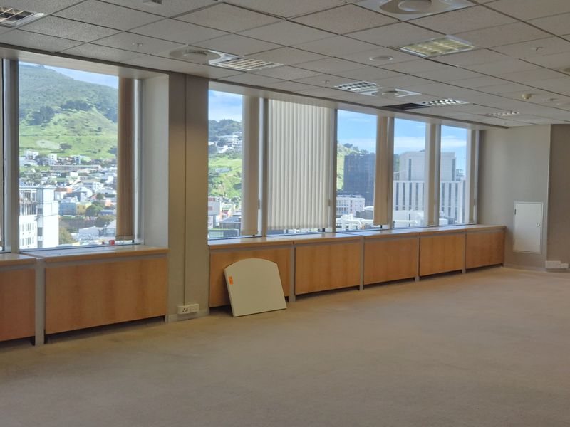 Spacious, empty office suite featuring large windows with city and mountain views, built-in cabinetry, carpeted floors, and a suspended ceiling with integrated lighting.