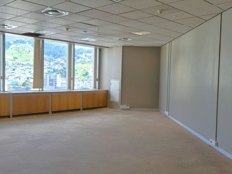 A spacious, empty office area featuring large windows with city views, suspended ceilings, recessed lighting, and built-in wooden cabinetry along the window perimeter.