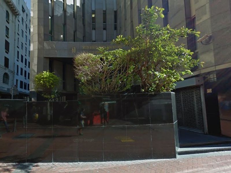 Street-level view of the office building entrance featuring a stone facade, integrated planter box, and security roller shutter access.