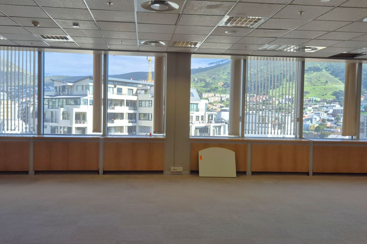 Spacious empty office area featuring large floor-to-ceiling windows with city views, suspended ceiling, and built-in wooden cabinetry along the perimeter.