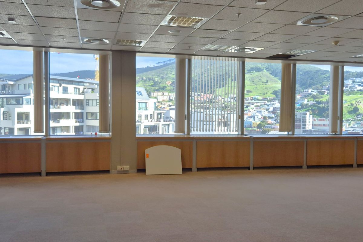 Spacious, empty office area featuring a suspended ceiling, carpeted floors, and expansive windows offering panoramic city and mountain views.