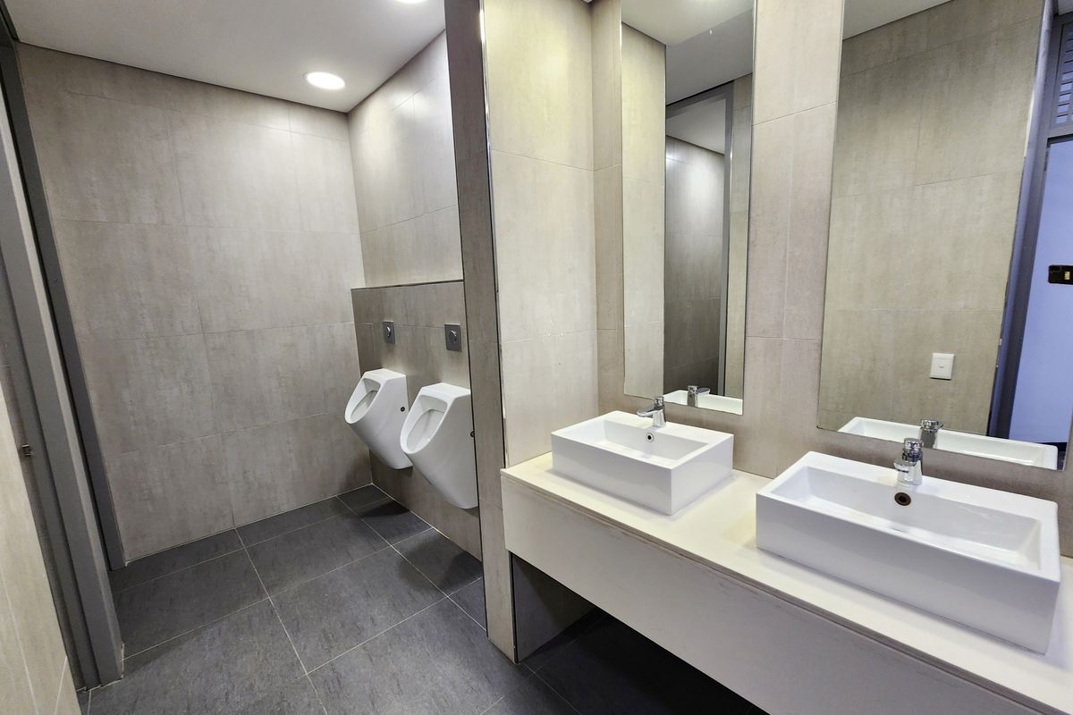 Modern office restroom featuring dual wall-mounted ceramic urinals and a double vanity with contemporary vessel sinks and large integrated mirrors.