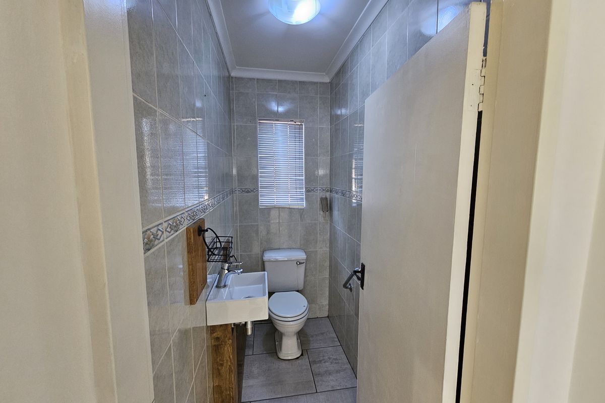 A compact office restroom featuring floor-to-ceiling wall tiles, a wall-mounted basin, and a standard toilet suite.