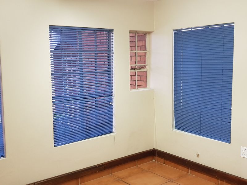 A vacant office space featuring ceramic tiled flooring, multiple windows with fitted venetian blinds, and neutral wall finishes.