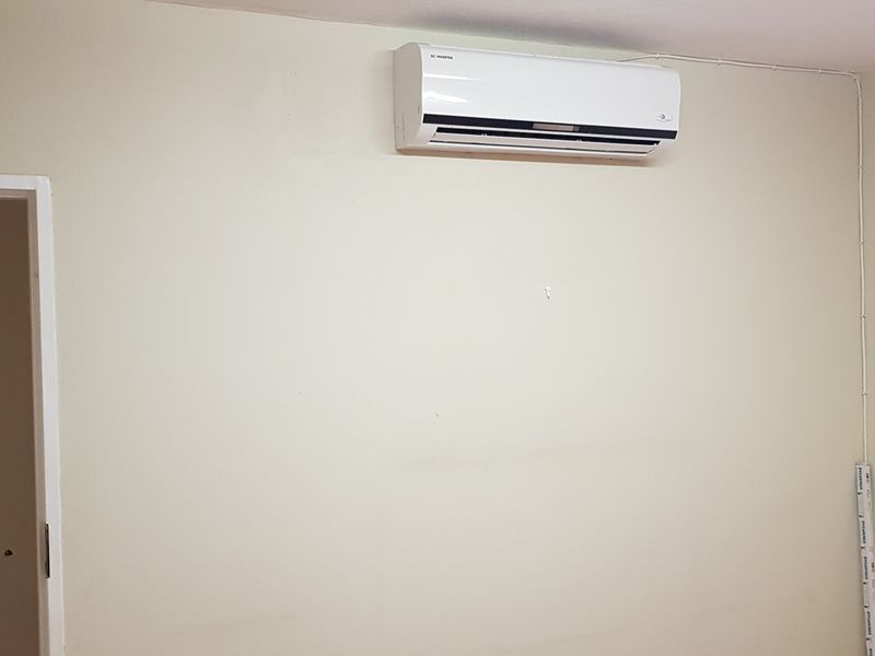 A simple, empty office space featuring a wall-mounted air conditioning unit and neutral wall finishes.