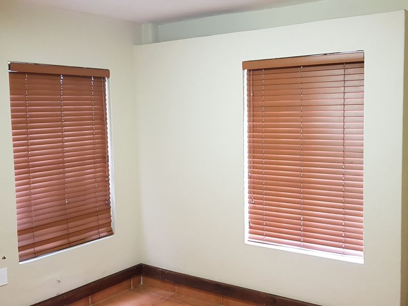 An empty office space featuring tiled flooring, neutral walls, and fitted wooden venetian blinds, providing a clean and functional workspace environment.