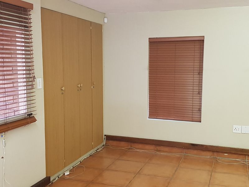 A vacant office space featuring tiled flooring, built-in wooden cupboards, and fitted wooden venetian blinds on the windows.