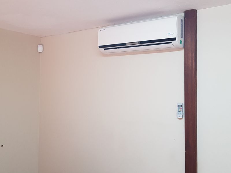 A clean, empty office space featuring a wall-mounted split-system air conditioner and security alarm sensor.