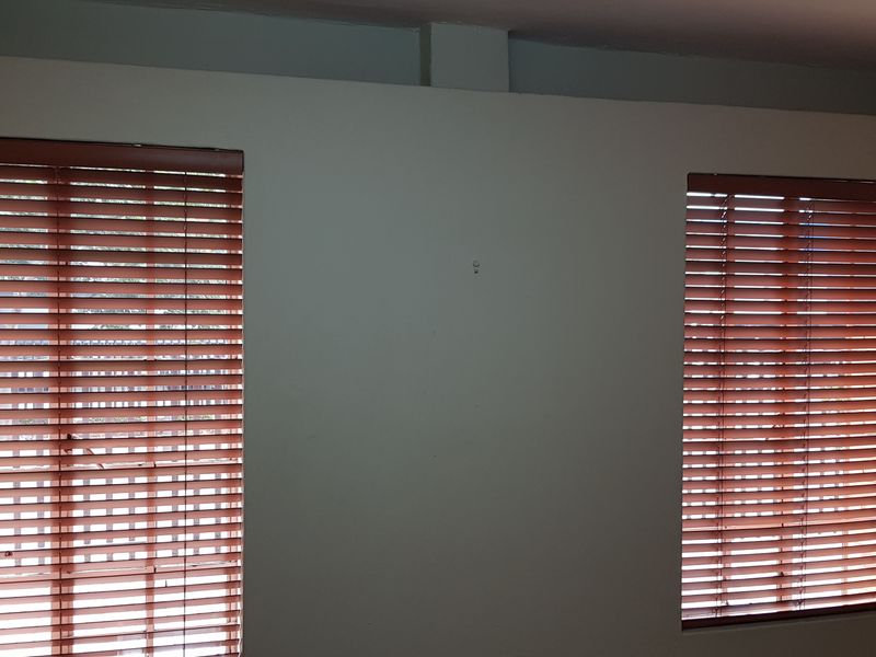 An empty office space featuring two windows fitted with wooden venetian blinds and neutral wall finishes.