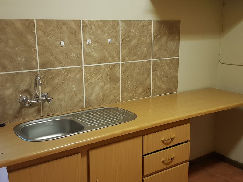 A functional scullery or utility area featuring a stainless steel sink, laminate countertop, built-in cabinetry, and tiled backsplash.