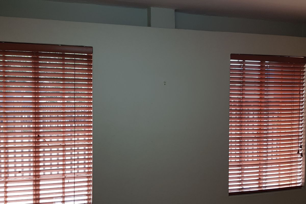 An empty office space featuring two windows fitted with wooden venetian blinds and neutral wall finishes.