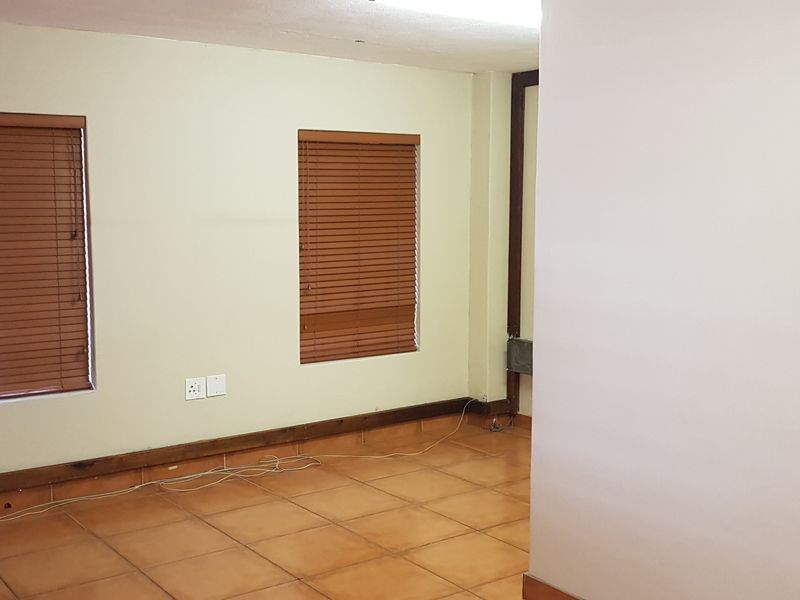 An empty office space featuring tiled flooring, wooden venetian blinds, and neutral wall finishes, suitable for a professional workspace setup.