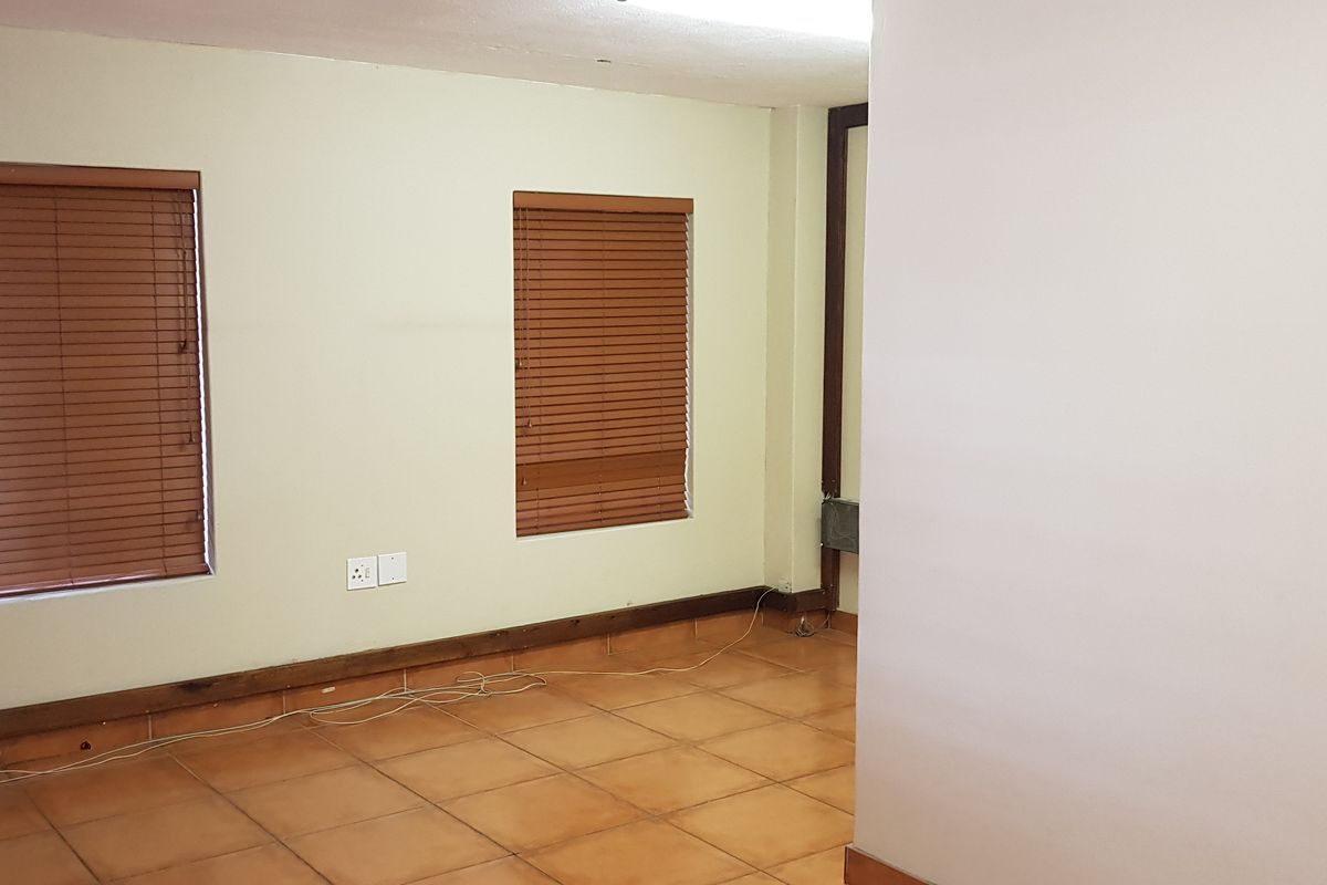 An empty office space featuring tiled flooring, wooden venetian blinds, and neutral wall finishes, suitable for a professional workspace setup.