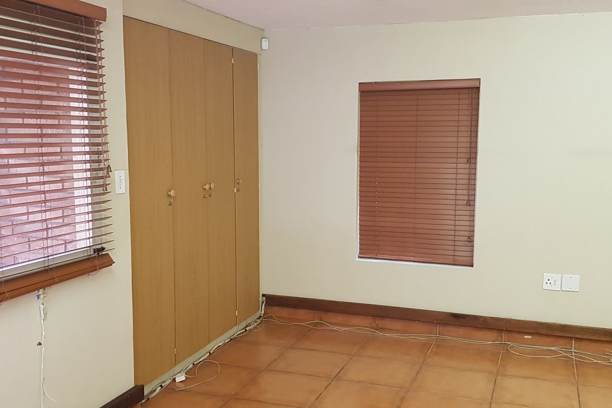 A vacant office space featuring tiled flooring, built-in wooden cupboards, and fitted wooden venetian blinds on the windows.