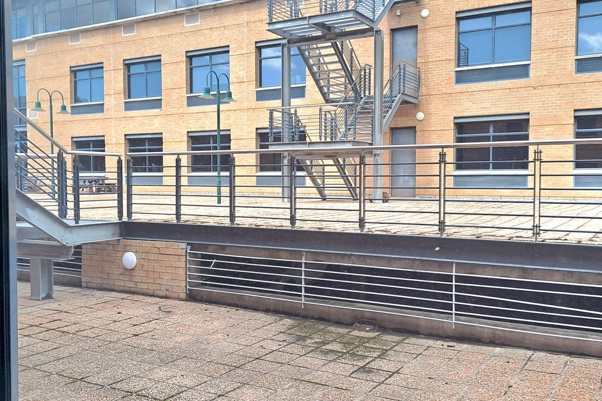 Exterior view of an office building featuring a paved terrace, metal fire escape staircase, and modern brick facade with large windows.